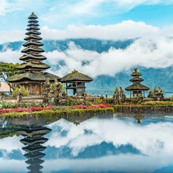 brown and green temple near body of water under blue and white cloudy sky during daytime