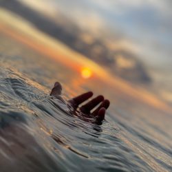 persons hand on water during sunset